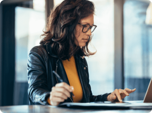Woman using a pen while typing on a computer